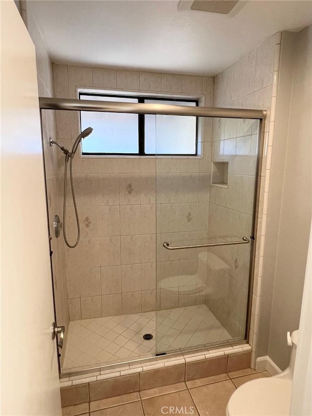 bathroom featuring tile patterned floors, toilet, and a shower with shower door