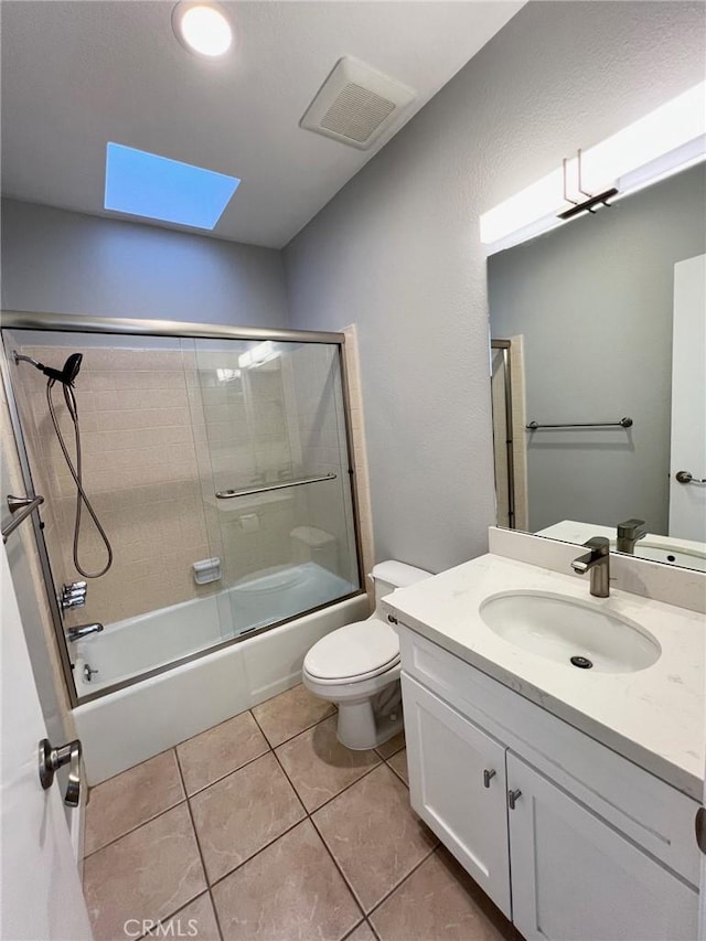 full bathroom featuring a skylight, bath / shower combo with glass door, vanity, tile patterned flooring, and toilet