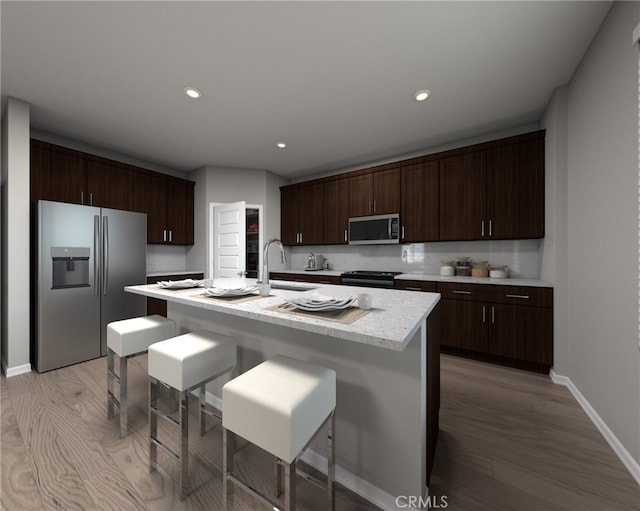 kitchen with dark brown cabinets, stainless steel appliances, a kitchen island with sink, sink, and light hardwood / wood-style flooring