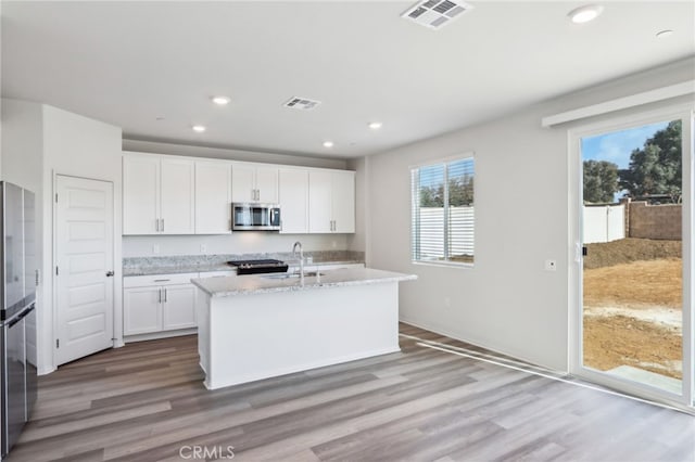 kitchen with white cabinetry, an island with sink, light stone counters, stainless steel appliances, and light wood-type flooring