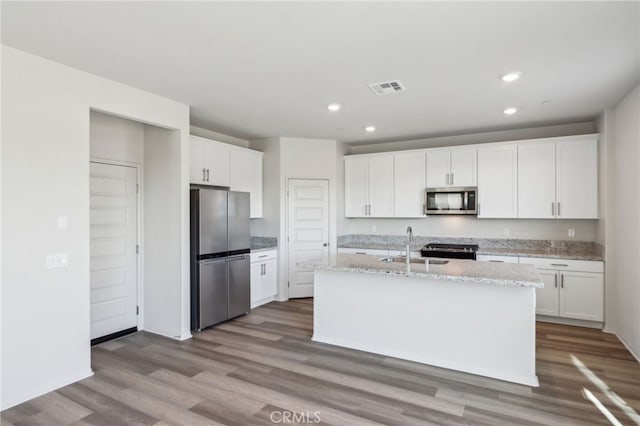 kitchen with appliances with stainless steel finishes, white cabinetry, an island with sink, sink, and light stone counters