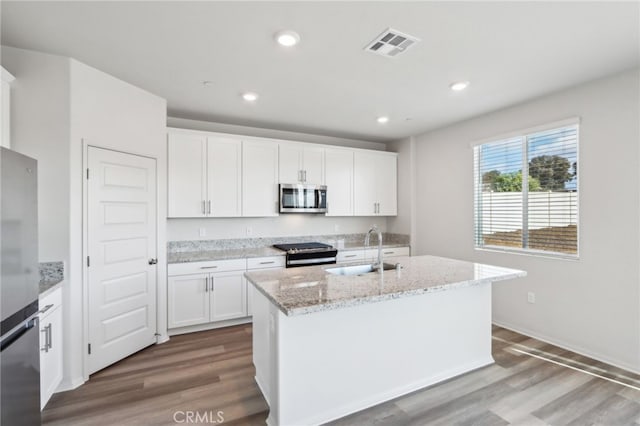 kitchen featuring appliances with stainless steel finishes, white cabinetry, sink, light stone countertops, and a center island with sink