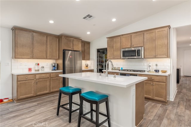 kitchen featuring a kitchen bar, stainless steel appliances, a center island with sink, hardwood / wood-style floors, and lofted ceiling