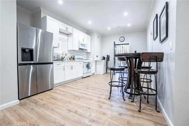 kitchen featuring crown molding, light hardwood / wood-style floors, white appliances, a breakfast bar area, and white cabinets