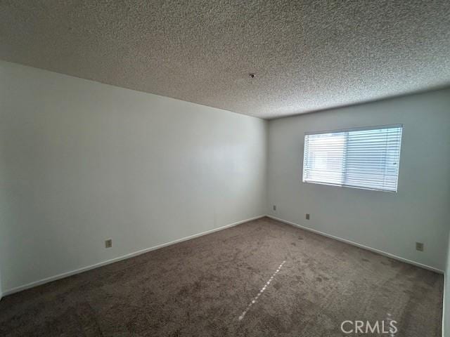 spare room with a textured ceiling and dark colored carpet