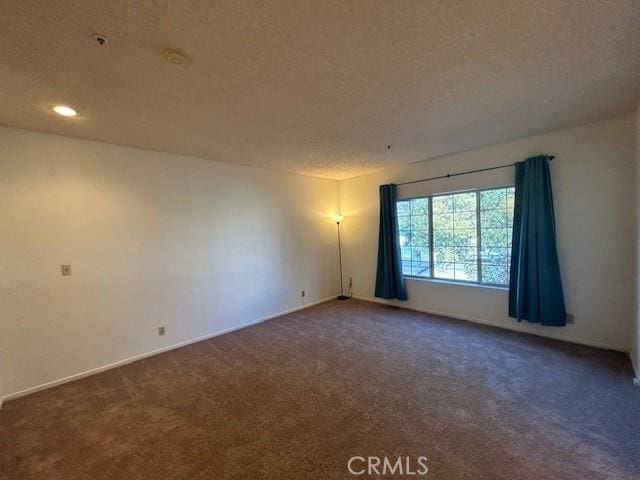 spare room featuring dark colored carpet and a textured ceiling