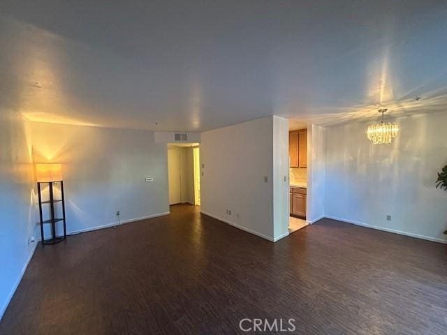 empty room with dark hardwood / wood-style flooring and a notable chandelier