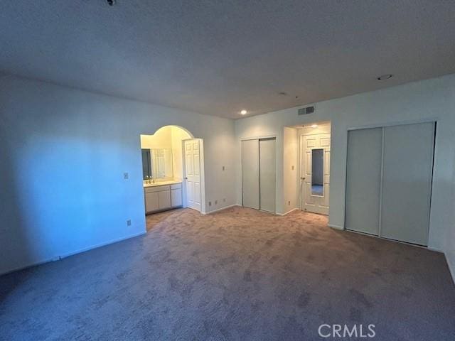 unfurnished bedroom with connected bathroom, two closets, and carpet floors