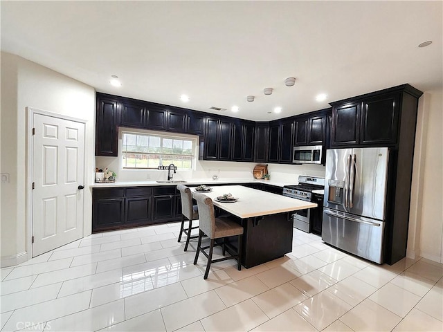 kitchen with a breakfast bar, light countertops, appliances with stainless steel finishes, a sink, and dark cabinetry