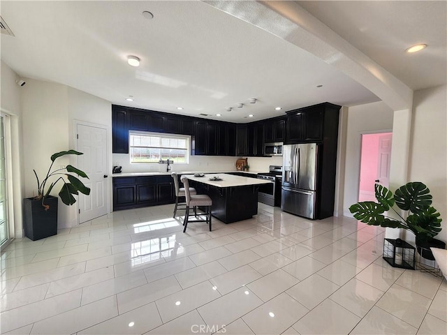 kitchen with light countertops, appliances with stainless steel finishes, a kitchen island, dark cabinets, and a kitchen bar