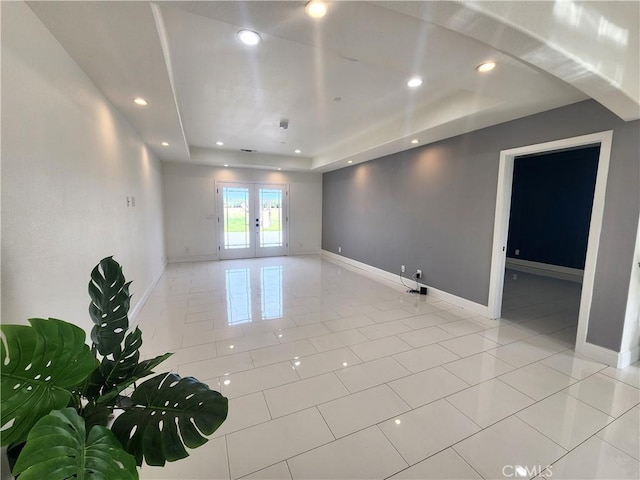 spare room featuring light tile patterned floors, baseboards, a raised ceiling, and french doors