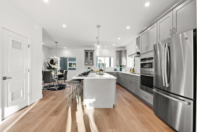 kitchen with a breakfast bar, decorative light fixtures, a center island, gray cabinets, and stainless steel appliances