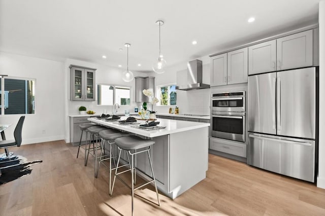 kitchen featuring stainless steel appliances, hanging light fixtures, gray cabinets, and wall chimney exhaust hood