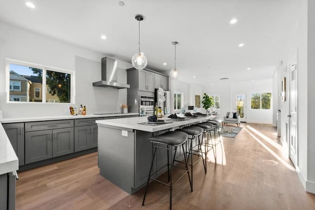 kitchen featuring gray cabinetry, a kitchen breakfast bar, hanging light fixtures, a kitchen island with sink, and wall chimney exhaust hood