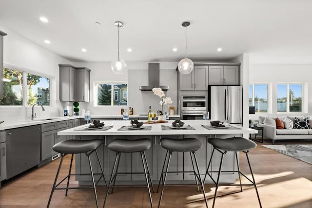 kitchen with gray cabinets, a kitchen island, appliances with stainless steel finishes, sink, and wall chimney range hood