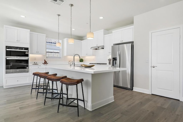 kitchen featuring a kitchen island with sink, white cabinetry, double oven, a kitchen bar, and stainless steel fridge with ice dispenser