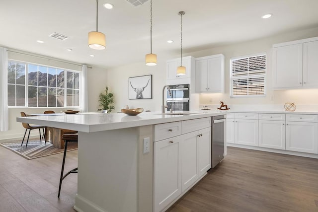 kitchen featuring white cabinets, hanging light fixtures, hardwood / wood-style flooring, a kitchen island with sink, and stainless steel double oven