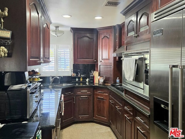 kitchen with tasteful backsplash, built in appliances, sink, and dark stone counters