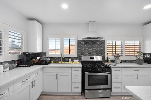 kitchen with sink, wall chimney range hood, tasteful backsplash, stainless steel range with gas cooktop, and white cabinets