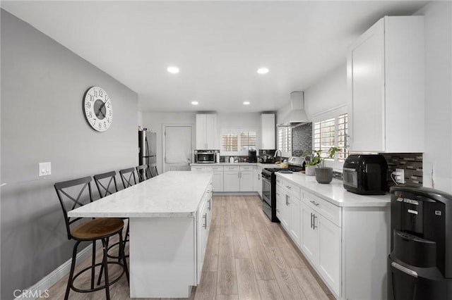 kitchen featuring white cabinetry, a center island, wall chimney exhaust hood, stainless steel appliances, and a kitchen breakfast bar