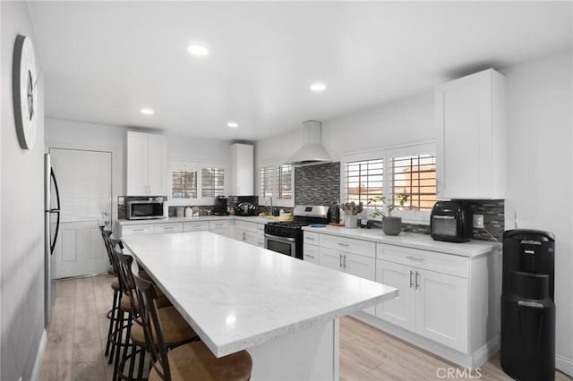 kitchen featuring a center island, premium range hood, appliances with stainless steel finishes, light hardwood / wood-style floors, and white cabinetry