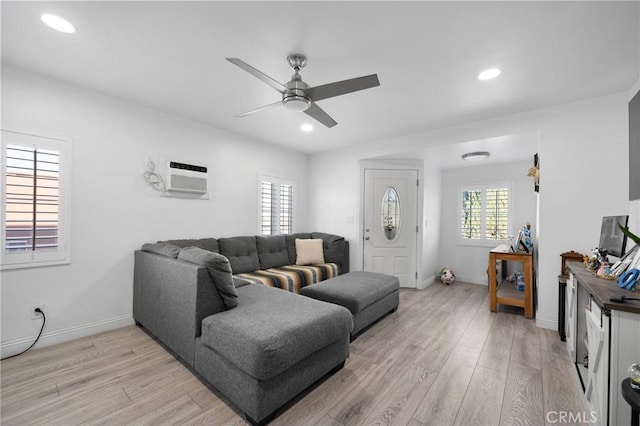 living room with a wall mounted AC, light hardwood / wood-style floors, and ceiling fan