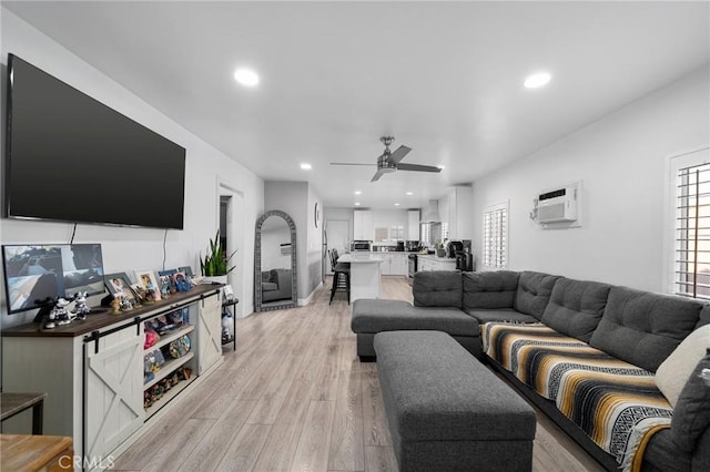 living room featuring ceiling fan, a wall mounted AC, and light hardwood / wood-style flooring