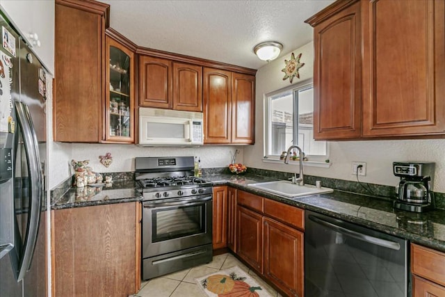 kitchen with appliances with stainless steel finishes, a textured ceiling, sink, light tile patterned floors, and dark stone countertops