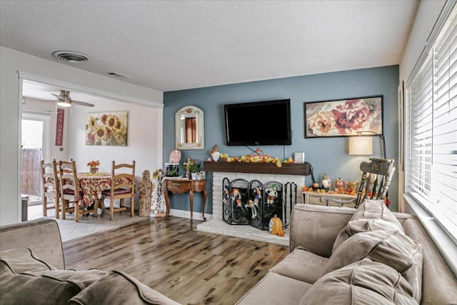 living room with a wealth of natural light, ceiling fan, light wood-type flooring, and a brick fireplace