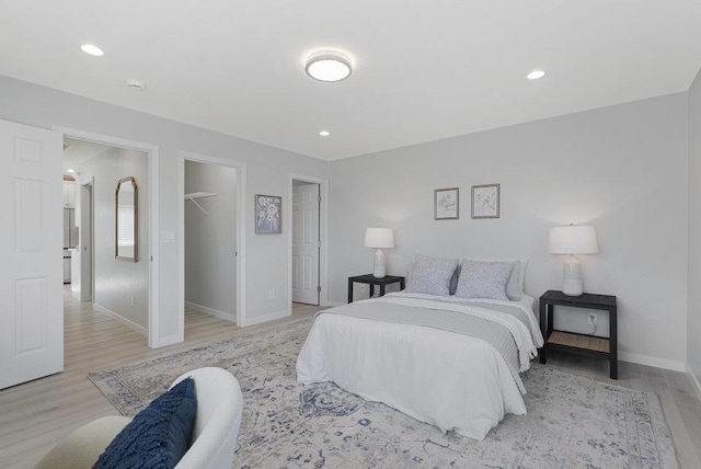 bedroom with a walk in closet, light wood-type flooring, and a closet