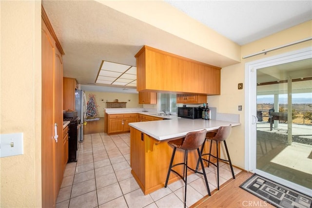 kitchen featuring sink, kitchen peninsula, light hardwood / wood-style floors, a breakfast bar area, and black appliances