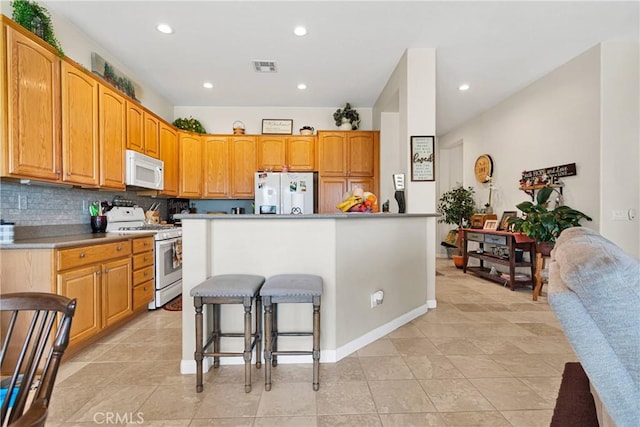 kitchen with a breakfast bar, backsplash, a center island, light tile patterned floors, and white appliances