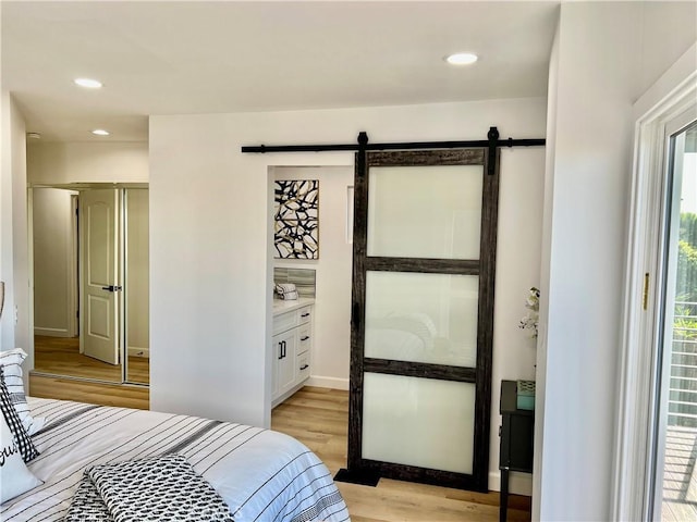 bedroom featuring a barn door, connected bathroom, and light hardwood / wood-style flooring