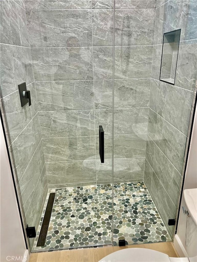 bathroom with hardwood / wood-style flooring, an enclosed shower, and toilet