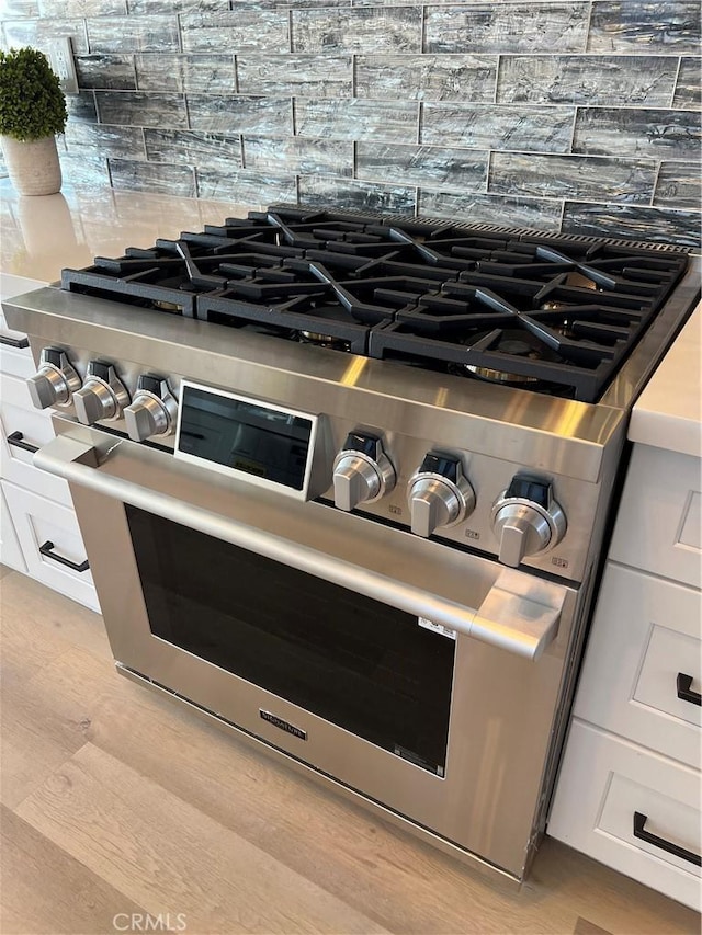 room details with white cabinets, backsplash, light hardwood / wood-style flooring, and double oven range