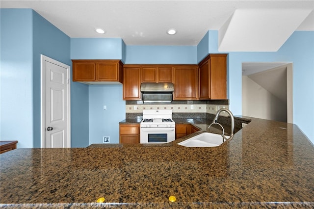 kitchen featuring white gas stove, dark stone countertops, backsplash, and sink