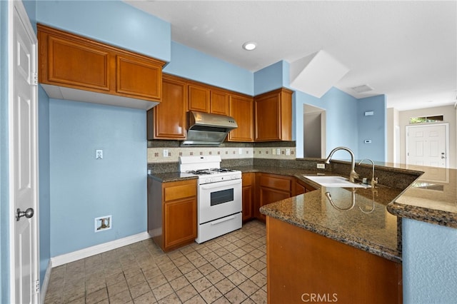 kitchen with kitchen peninsula, decorative backsplash, sink, and white gas range