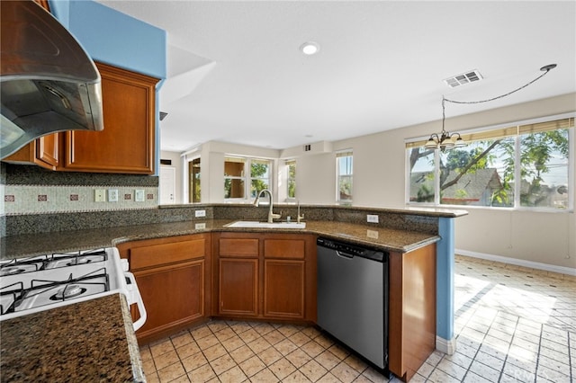 kitchen featuring dishwasher, exhaust hood, dark stone countertops, sink, and a notable chandelier