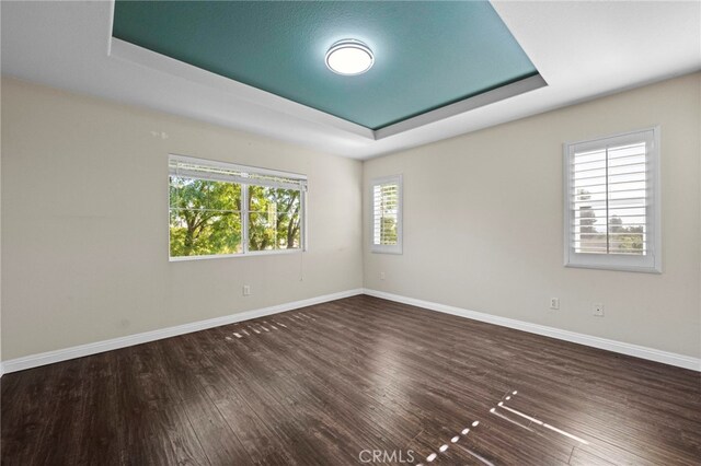 empty room with dark hardwood / wood-style floors and a tray ceiling