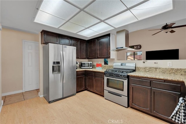 kitchen with wall chimney exhaust hood, ceiling fan, dark brown cabinets, light hardwood / wood-style floors, and stainless steel appliances