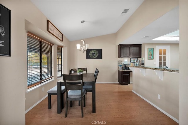 dining area with a notable chandelier, vaulted ceiling, and light hardwood / wood-style flooring