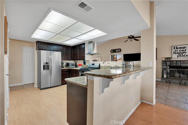 kitchen with vaulted ceiling, dark brown cabinets, stainless steel appliances, and wall chimney range hood