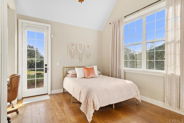 bedroom featuring access to outside, multiple windows, wood-type flooring, and vaulted ceiling