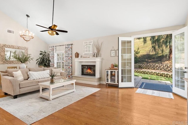 living room with hardwood / wood-style flooring, ceiling fan with notable chandelier, lofted ceiling, and french doors