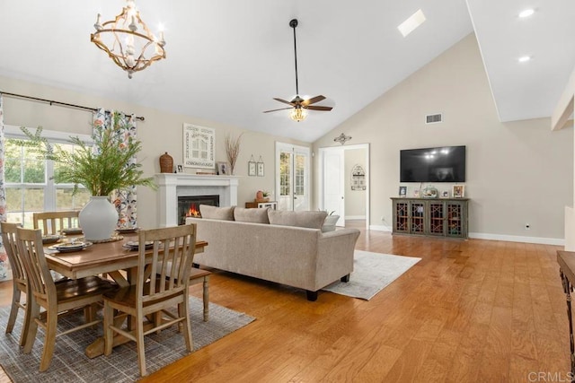 living room with ceiling fan with notable chandelier, light wood-type flooring, and high vaulted ceiling