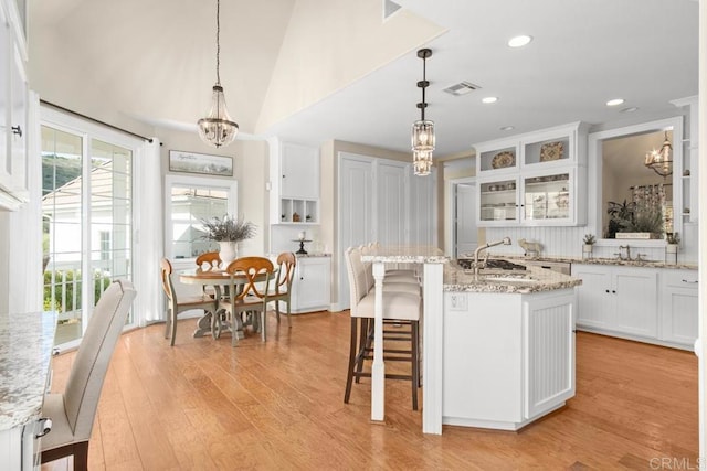 kitchen with white cabinets, pendant lighting, light wood-type flooring, and a center island with sink