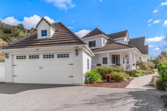 view of front of property with covered porch, a tiled roof, aphalt driveway, and an attached garage