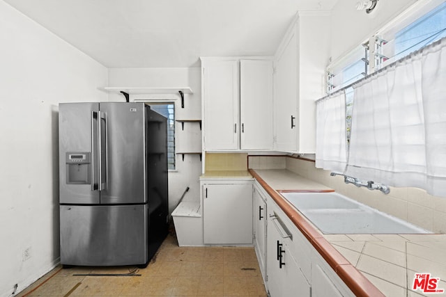 kitchen with tile countertops, stainless steel fridge, and white cabinetry