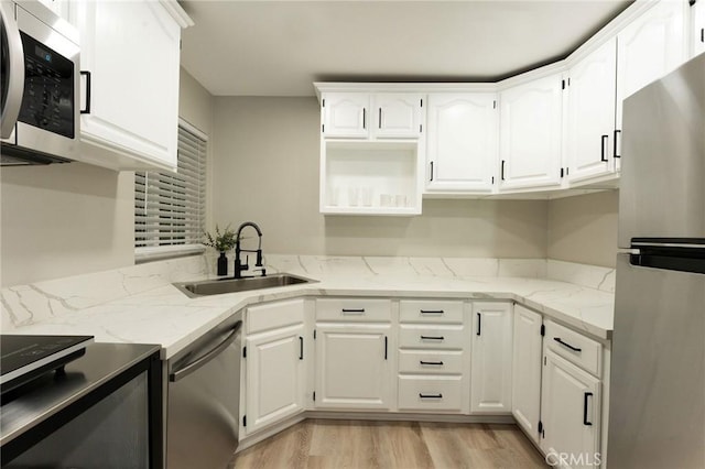 kitchen with light stone countertops, appliances with stainless steel finishes, sink, light hardwood / wood-style floors, and white cabinetry