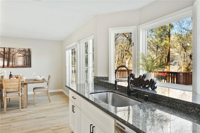 kitchen featuring dark stone countertops, white cabinetry, sink, and light hardwood / wood-style floors